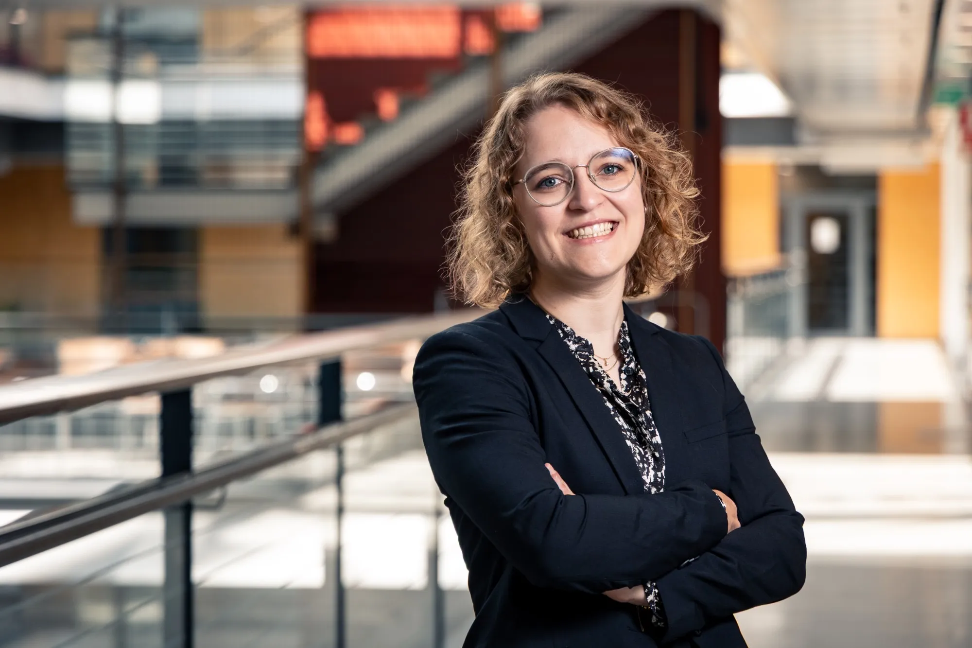 Alexandra Dahlberg in a dark blazer, arms crossed, smiling in a university atrium
