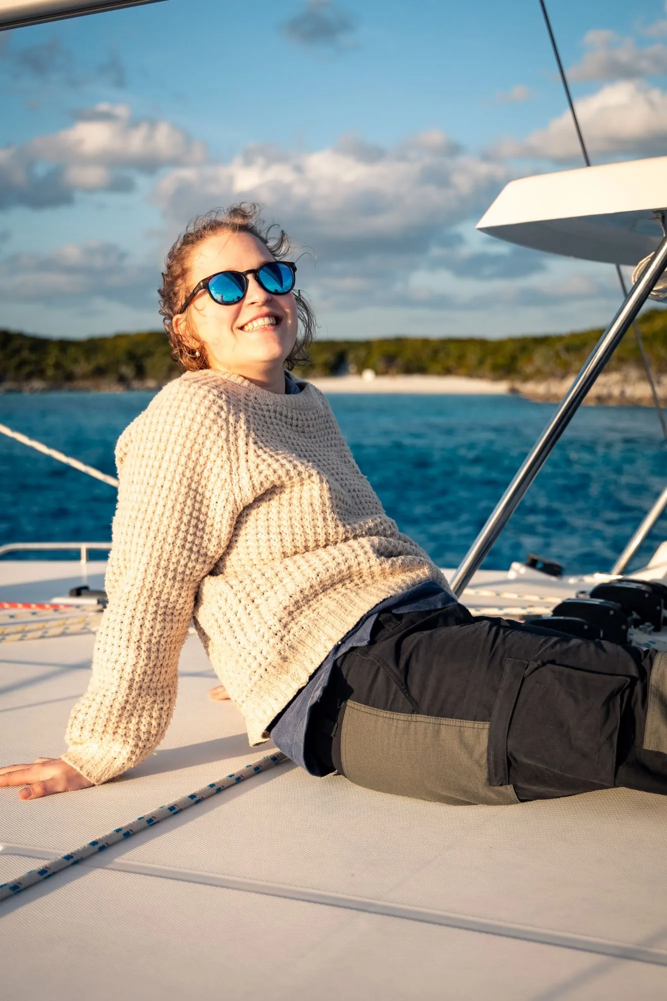 Alexandra in a knitted sweater and sunglasses, smiling on the deck of a sailing boat